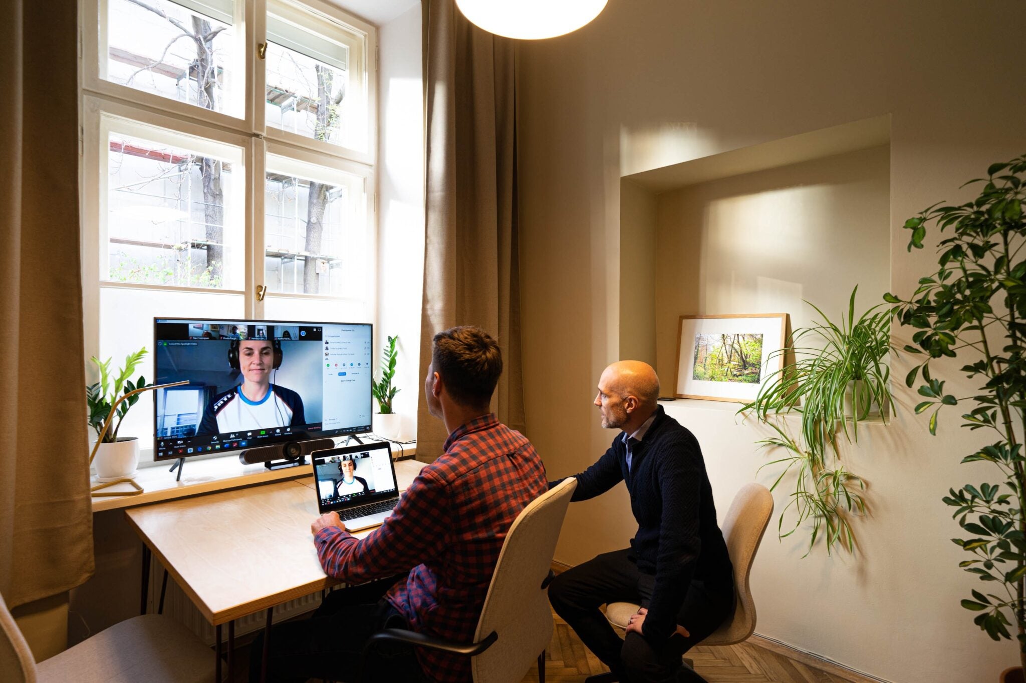 two men sitting at a desk talking to a coworker virtually